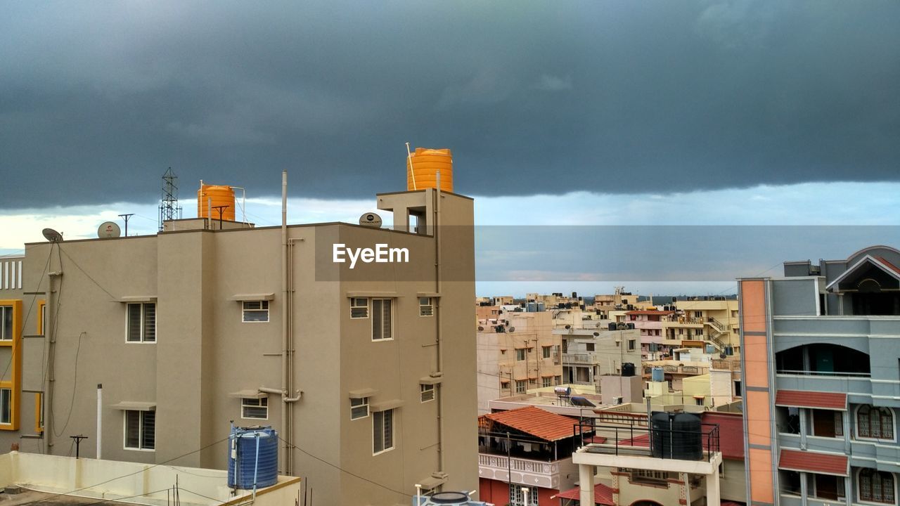 Yellow water tower on building against cloudy sky in city