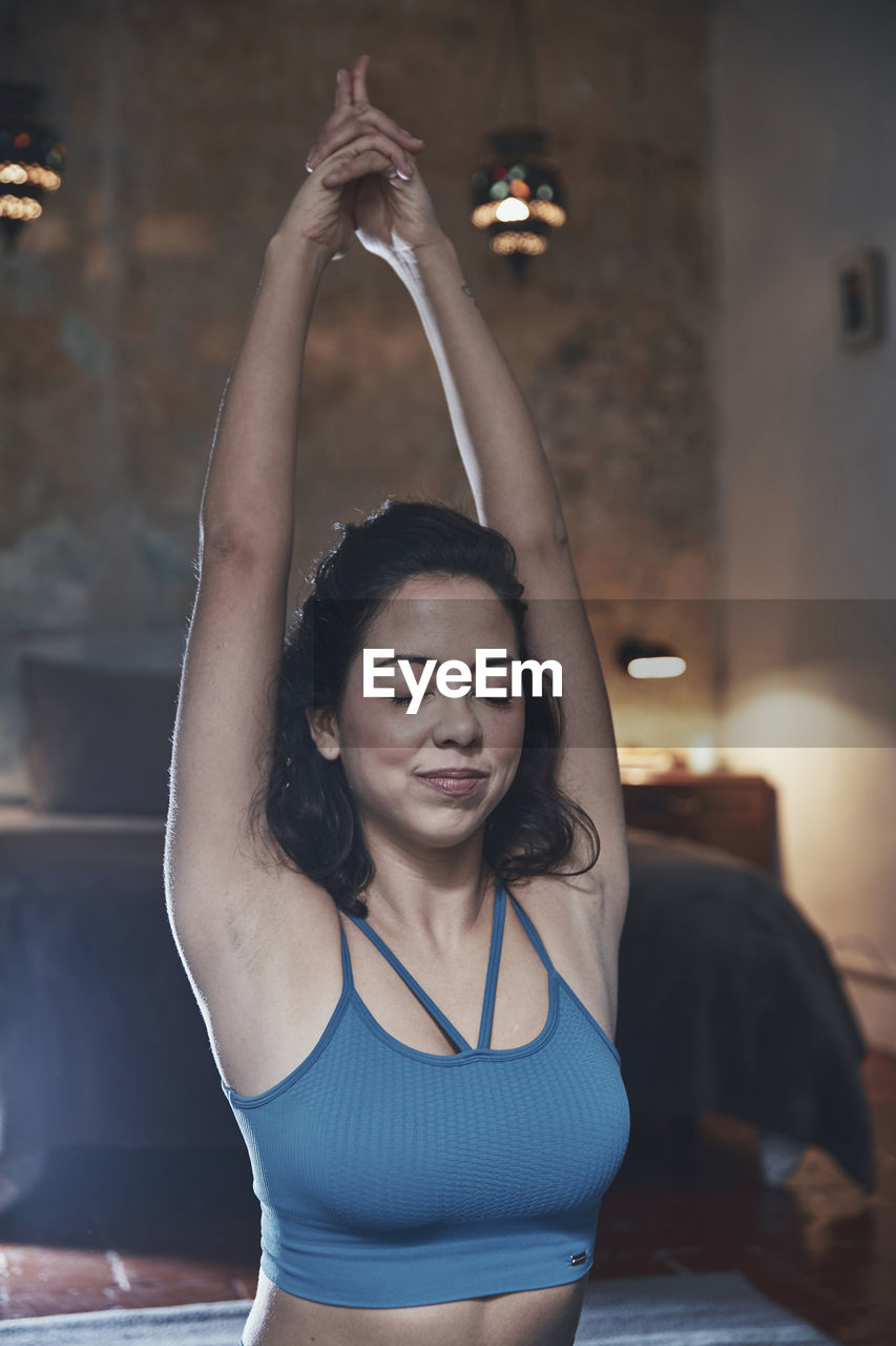 Beautiful woman exercising while sitting on bed at home