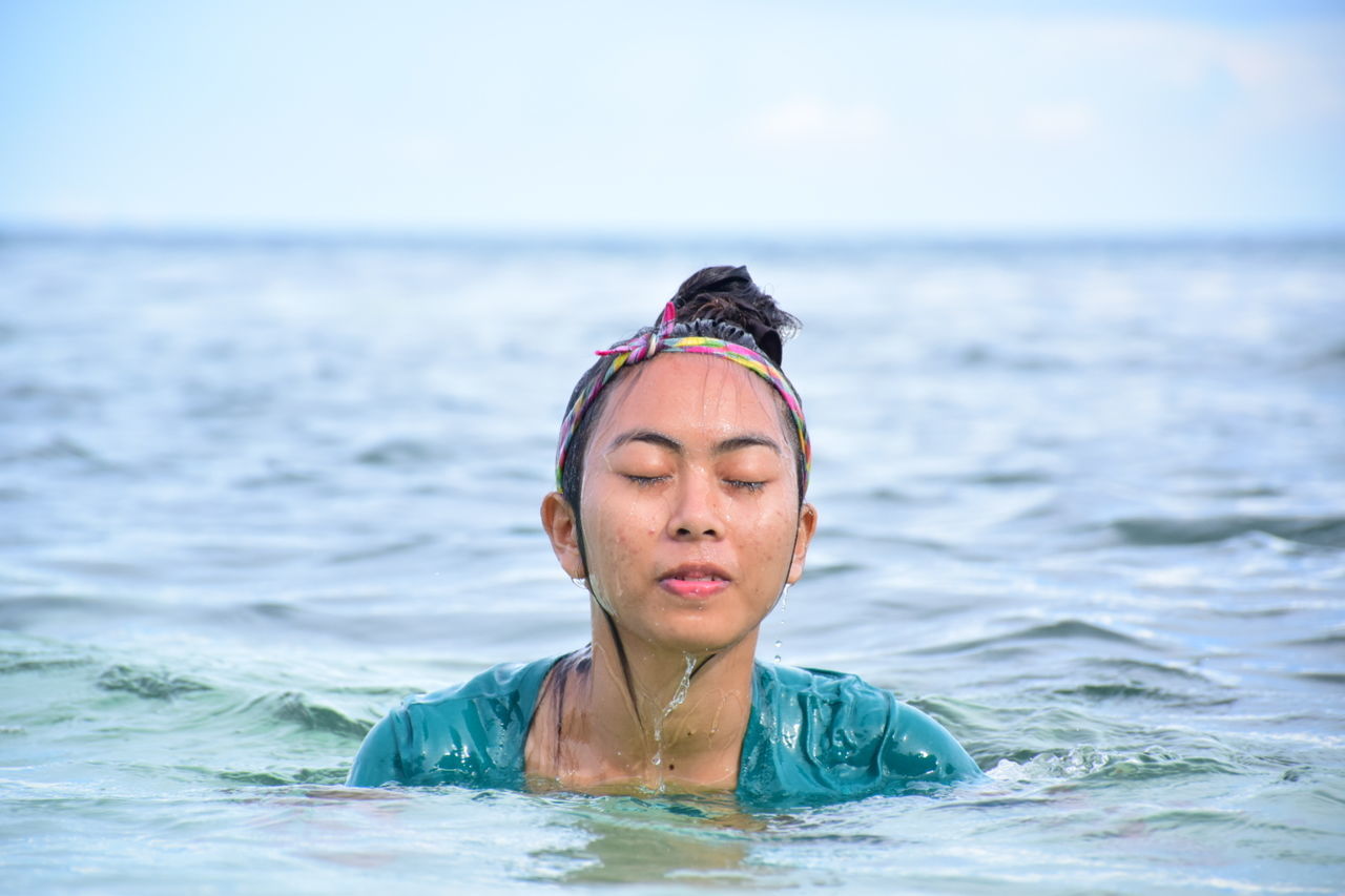 Young woman with eyes closed swimming in sea against sky
