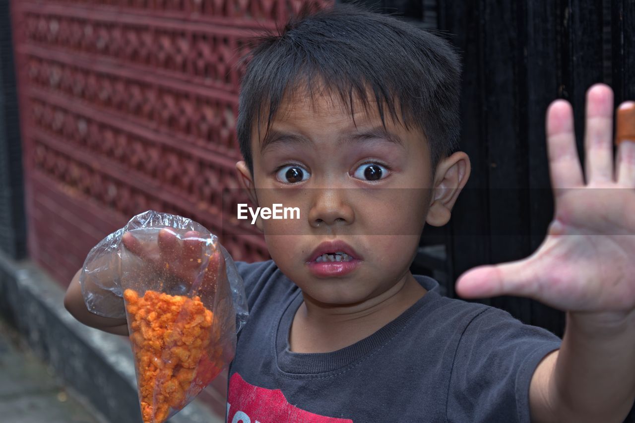 Close-up portrait of shocked boy holding snacks in plastic