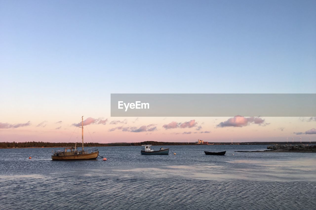 Sailboats in sea against sky during sunset