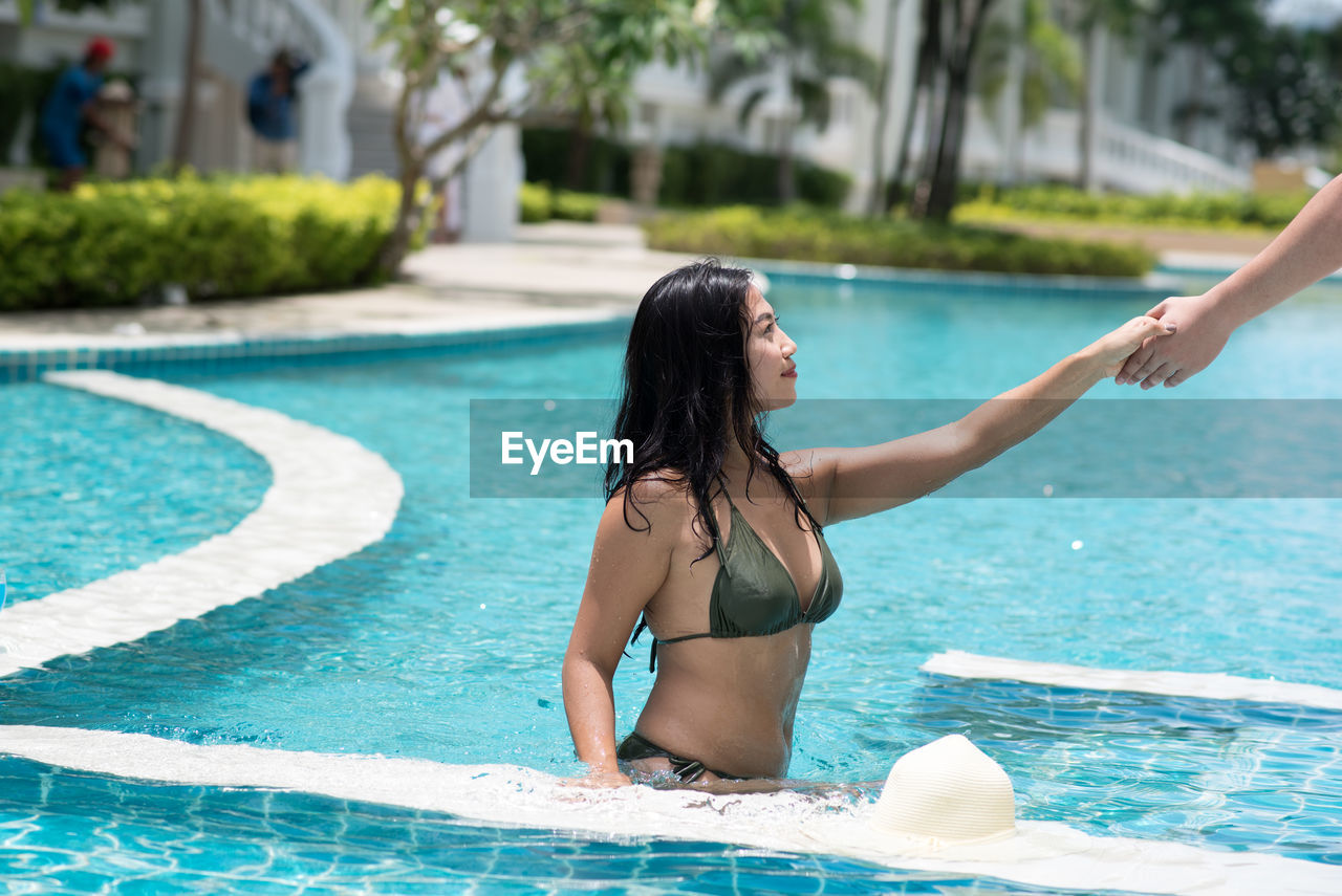 Cropped hand assisting young woman out of swimming pool