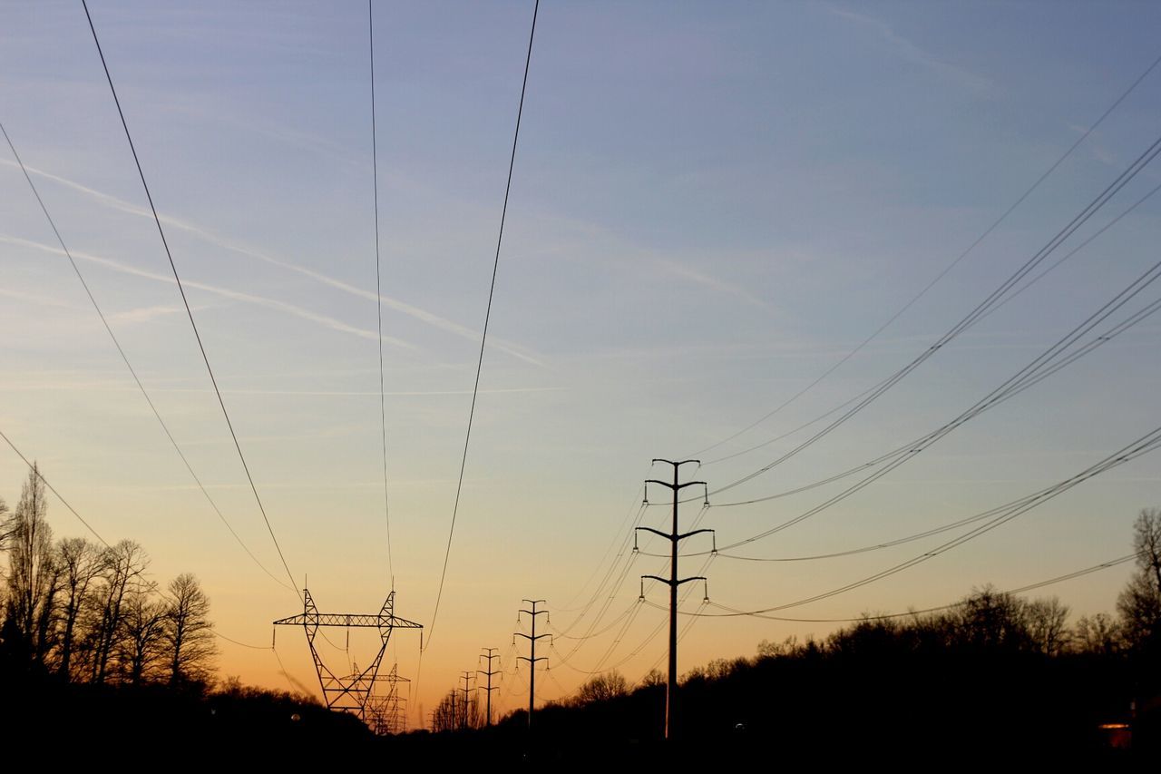 Low angle view of silhouette trees and electricity pylons against sky at sunset