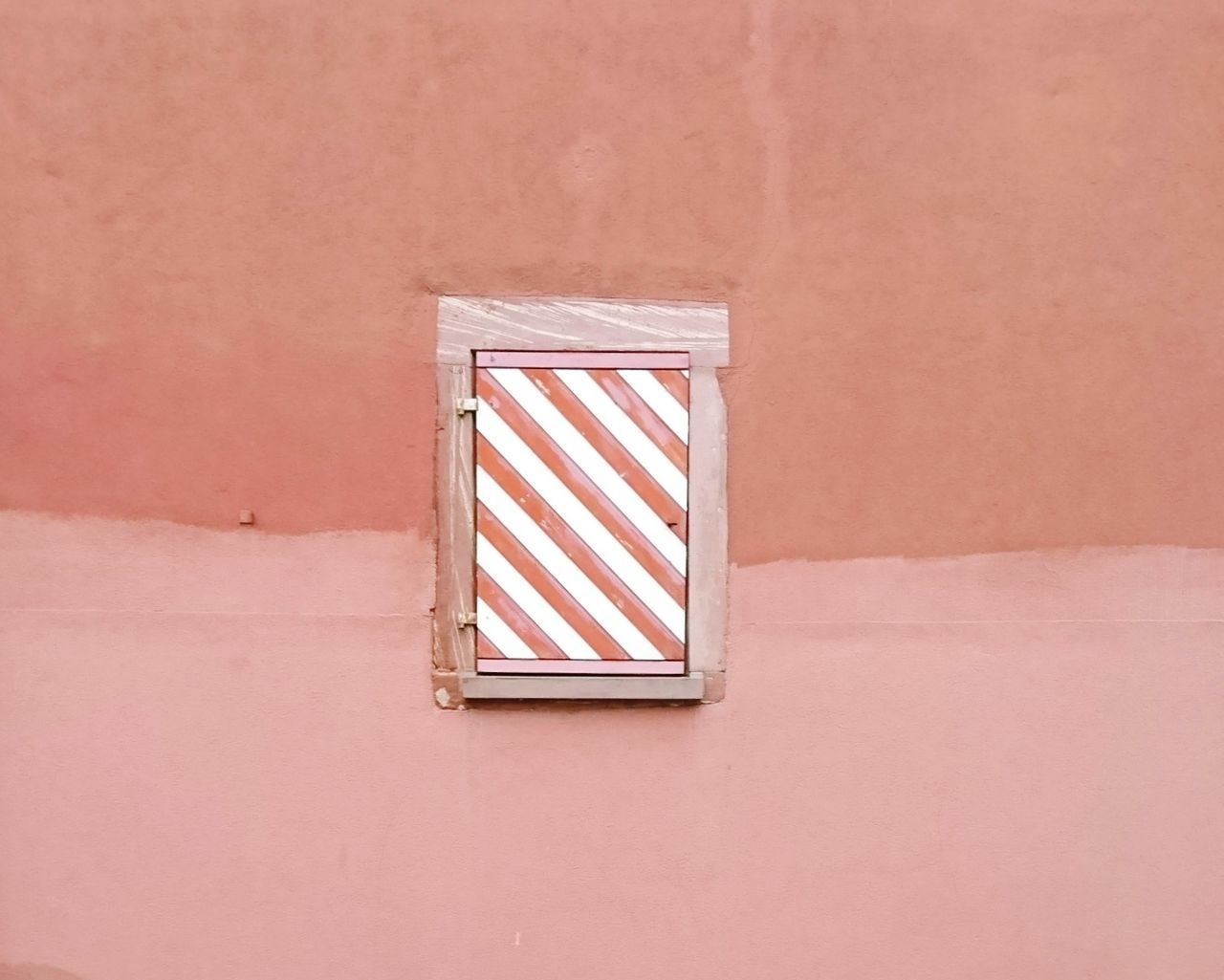 Closed window amidst coral colored wall