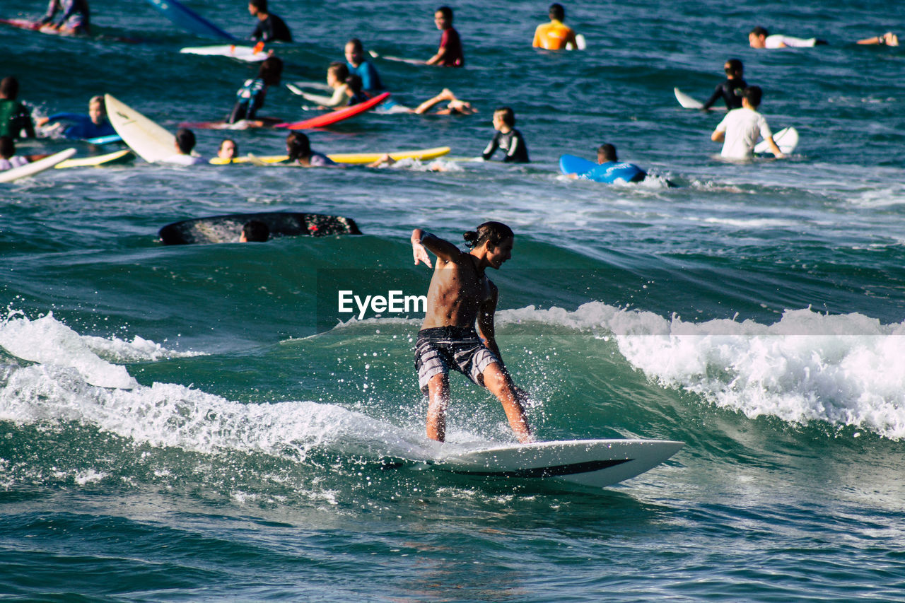 REAR VIEW OF PEOPLE SURFING IN SEA