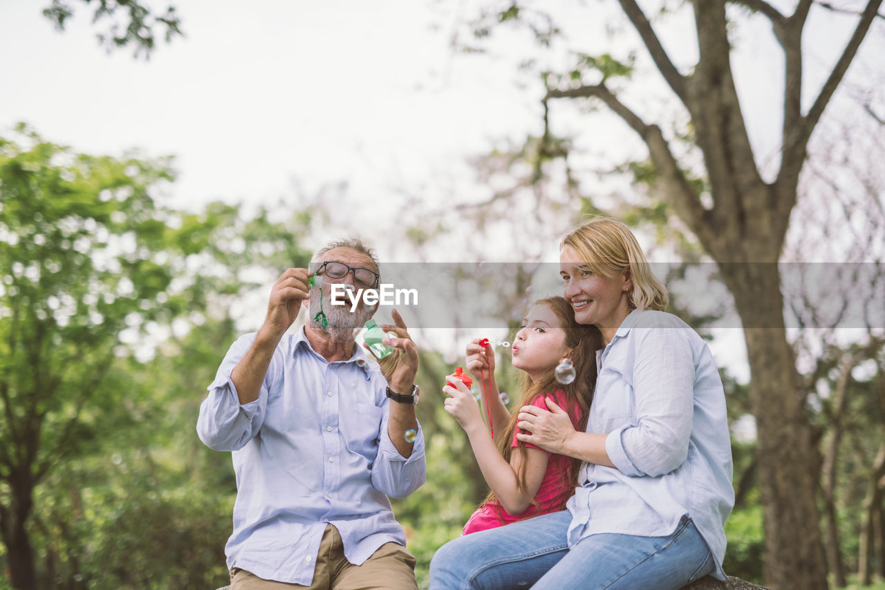 Happy multi-generation family blowing bubbles in park