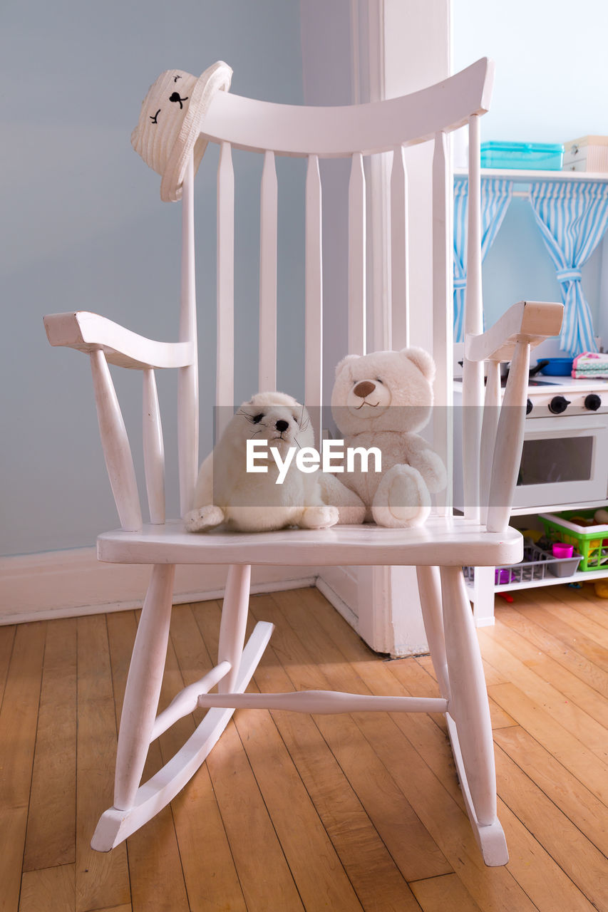  plush toys on white wooden rocker in child bedroom, with play oven in the background