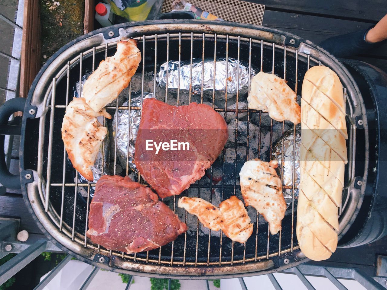 Directly above shot of meat and breads on barbecue grill by railing in yard