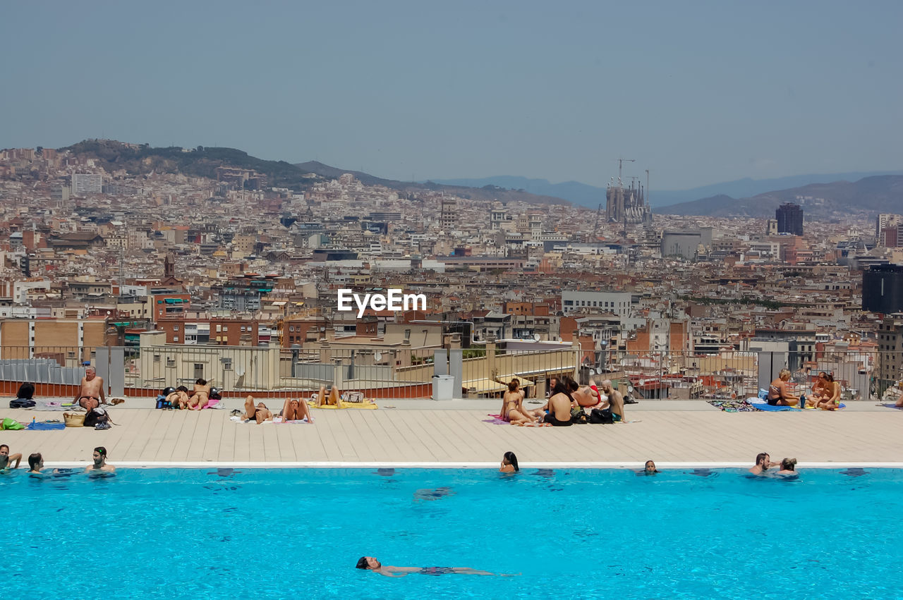 PEOPLE AT SWIMMING POOL AGAINST BUILDINGS IN CITY