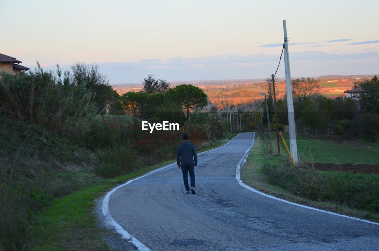 REAR VIEW OF MAN WALKING ON ROAD AMIDST TREES