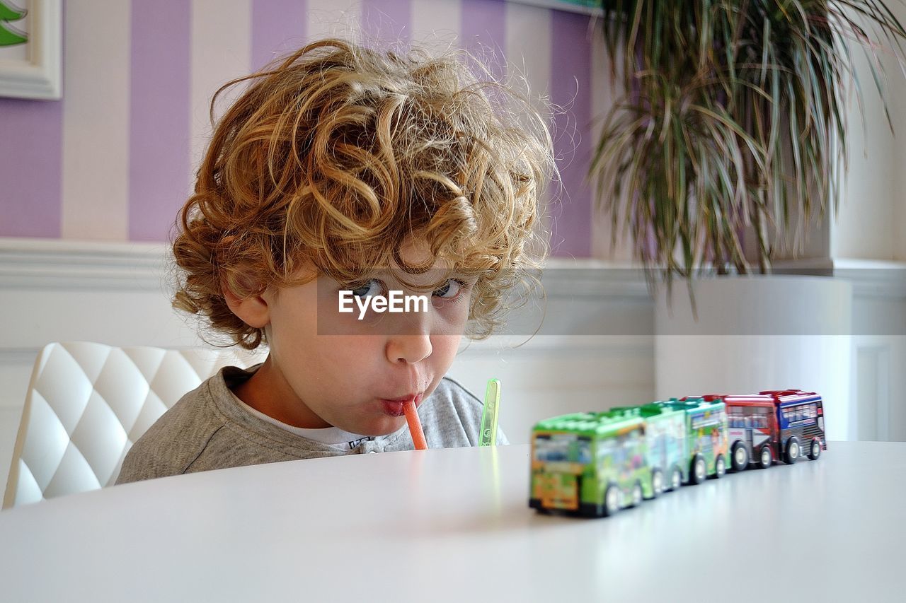 Portrait of boy drinking while sitting on table at home