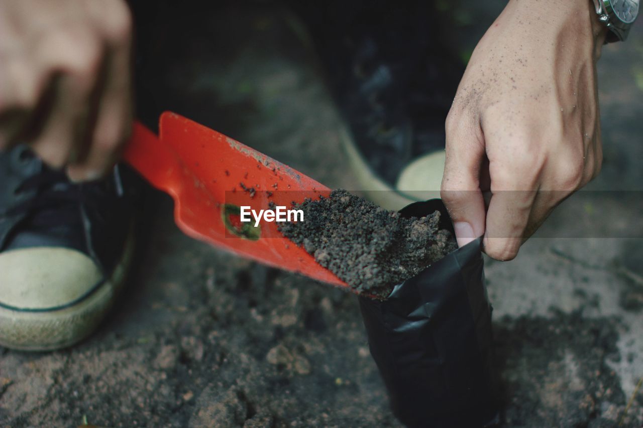 Low section of person filling plastic bag with soil on field