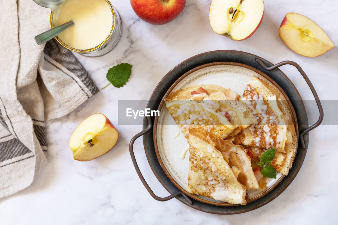 Homemade sweet crepes with apples and condensed milk on a marble tabletop. top view flat lay.
