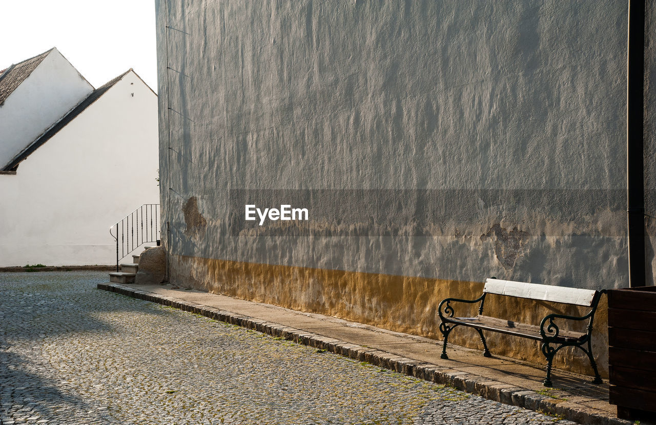 EMPTY BENCH ON WALL BY STREET