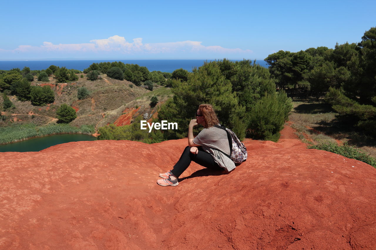 REAR VIEW OF SENIOR MAN SITTING ON LAND AGAINST SKY