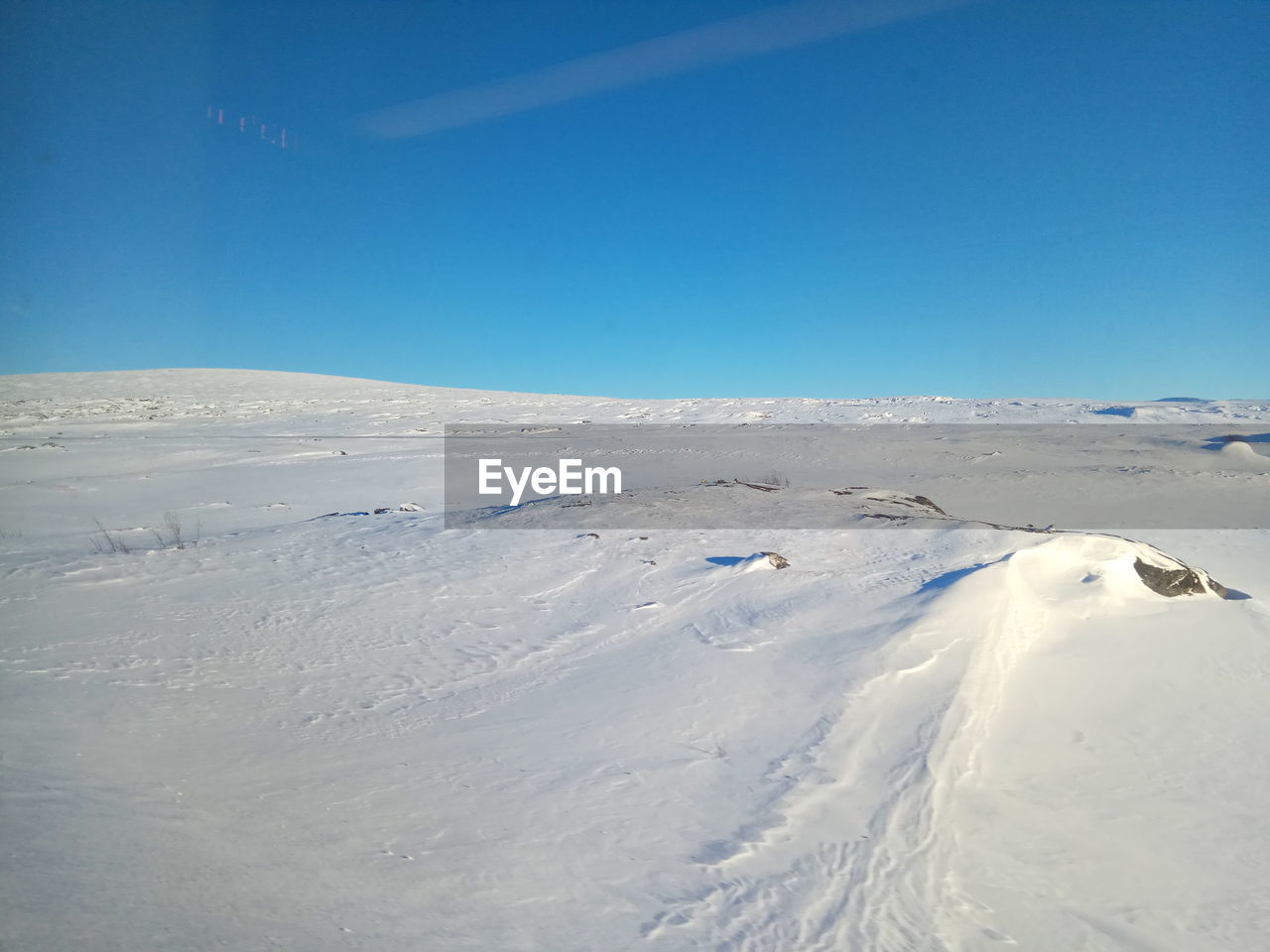 Snow covered landscape against clear blue sky