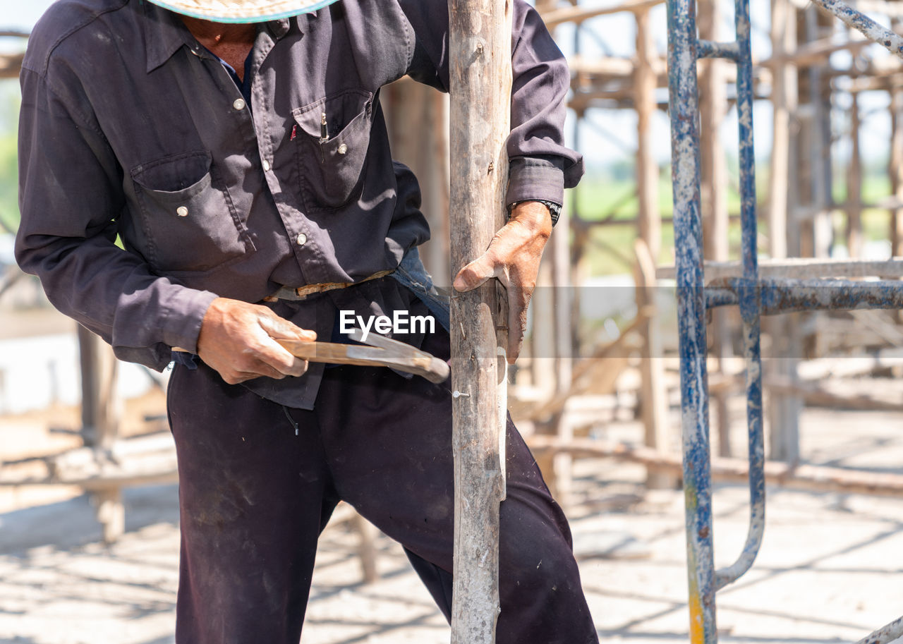 Worker hit nail on wooden stick for support scaffolding second floor in construction site.
