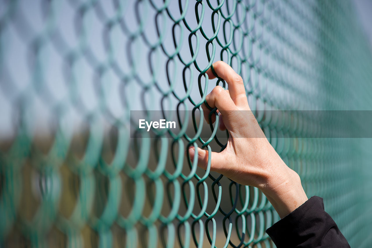 Cropped image of hand on chainlink fence