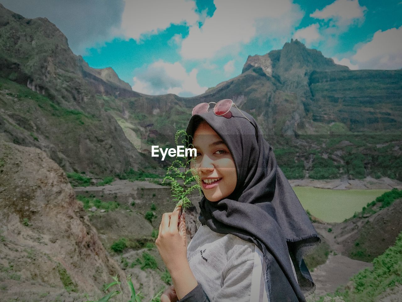 Portrait of smiling woman holding plant against mountain range