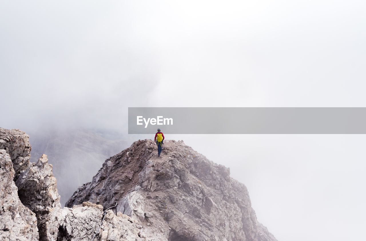 Rear view of person on rock in mountains against sky