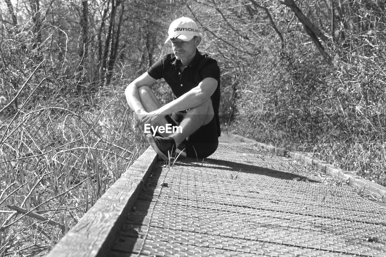 FULL LENGTH PORTRAIT OF YOUNG MAN SITTING ON WOODEN FLOOR