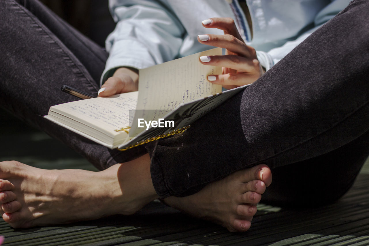 Low section of woman reading book while sitting indoors