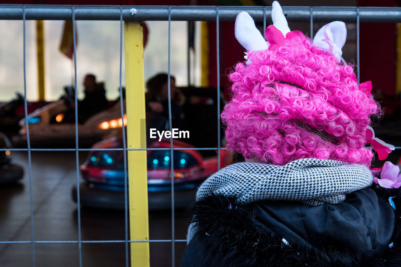 Rear view of person wearing pink wig while standing by gate