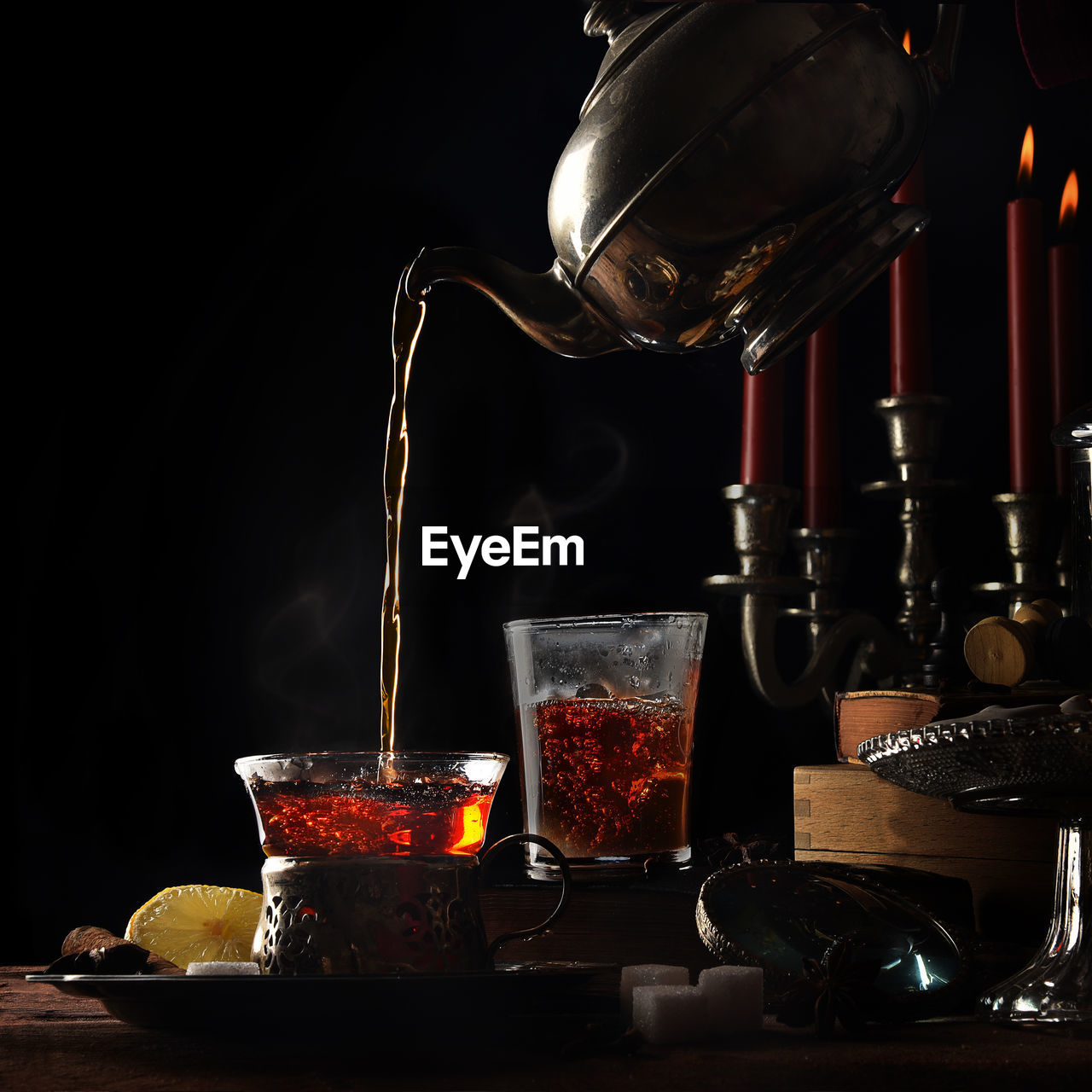 Teapot pouring tea in cup on table against black background