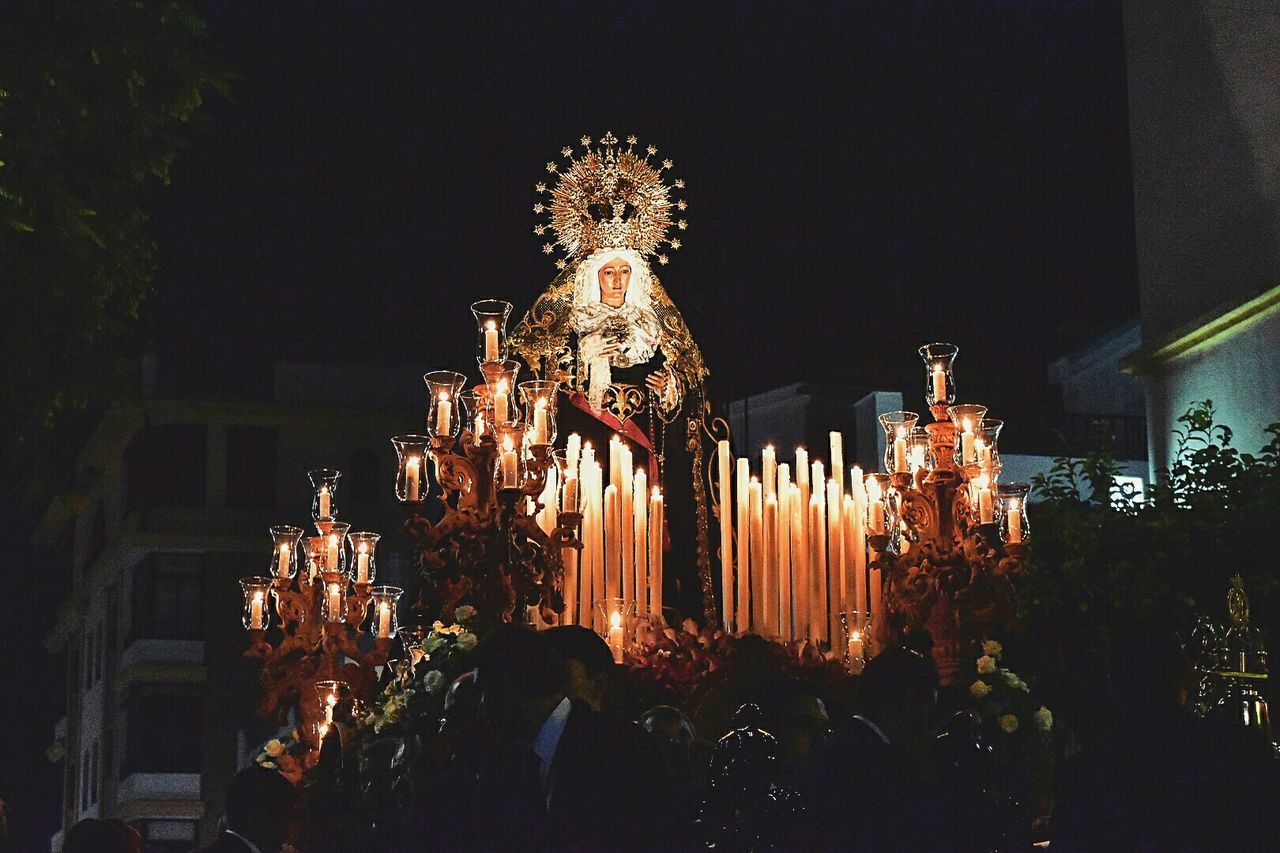 Low angle view of illuminated candles by virgin mary against buildings