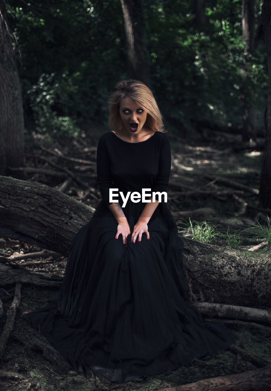 Woman with blind eyes sitting on tree in forest
