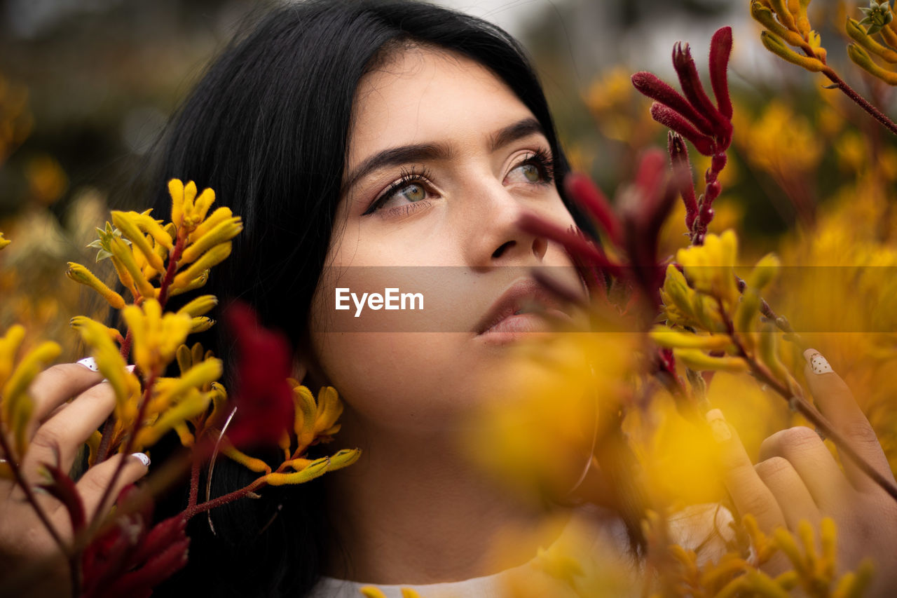 CLOSE-UP PORTRAIT OF WOMAN WITH RED YELLOW FLOWERING PLANTS