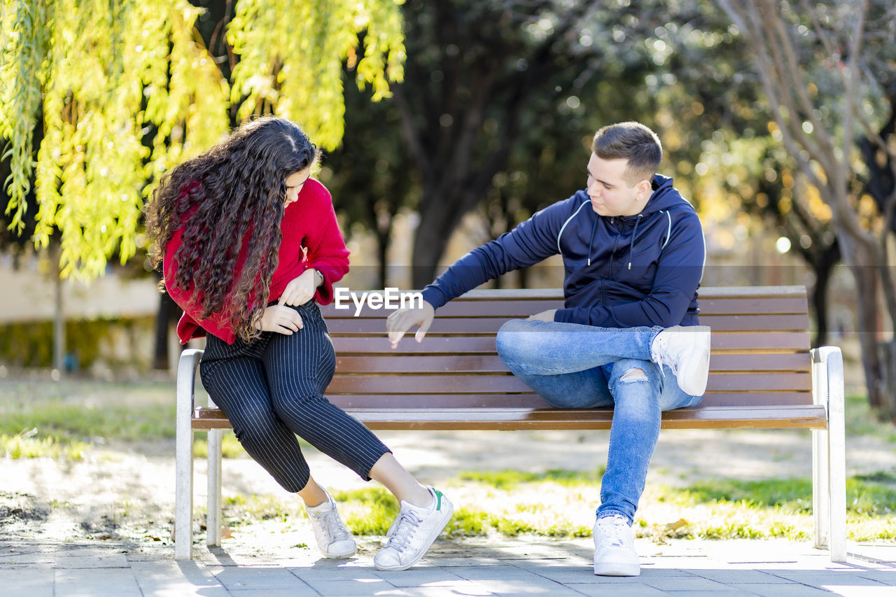 Full length of couple sitting on bench at park