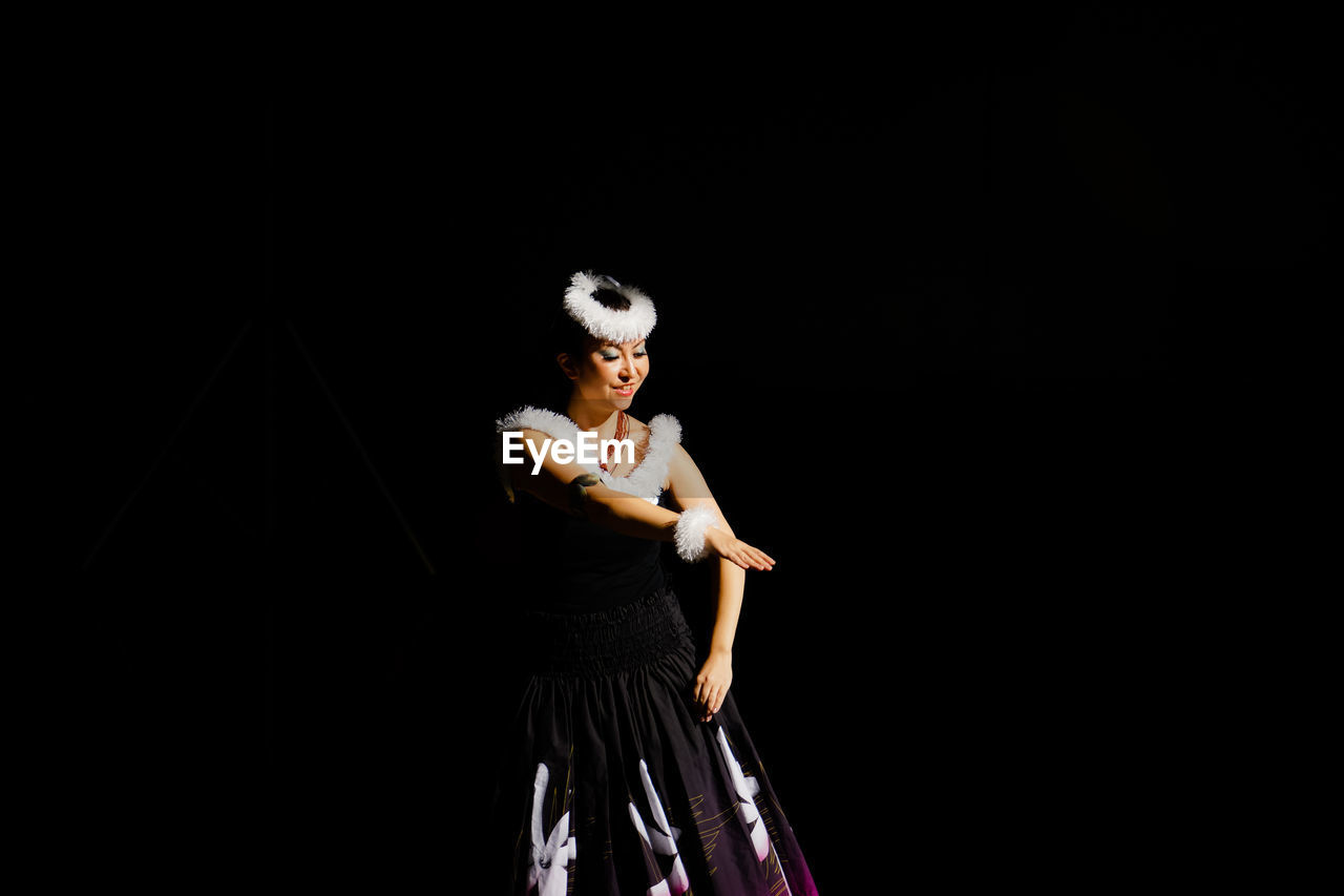 Woman wearing traditional clothing while doing hula dancing against black background