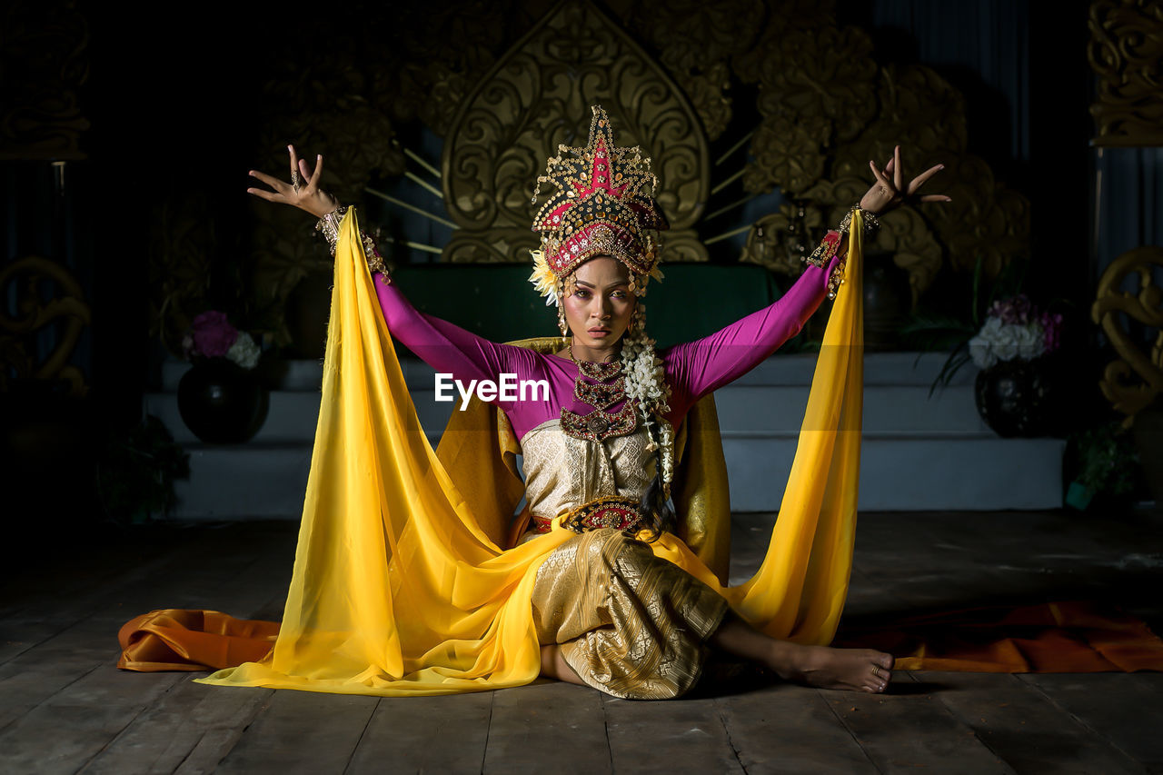 Portrait of woman in traditional clothing sitting against decoration