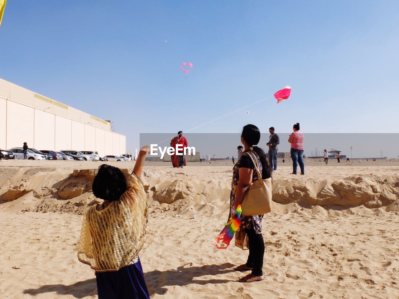 REAR VIEW OF PEOPLE STANDING ON BEACH AGAINST CLEAR SKY