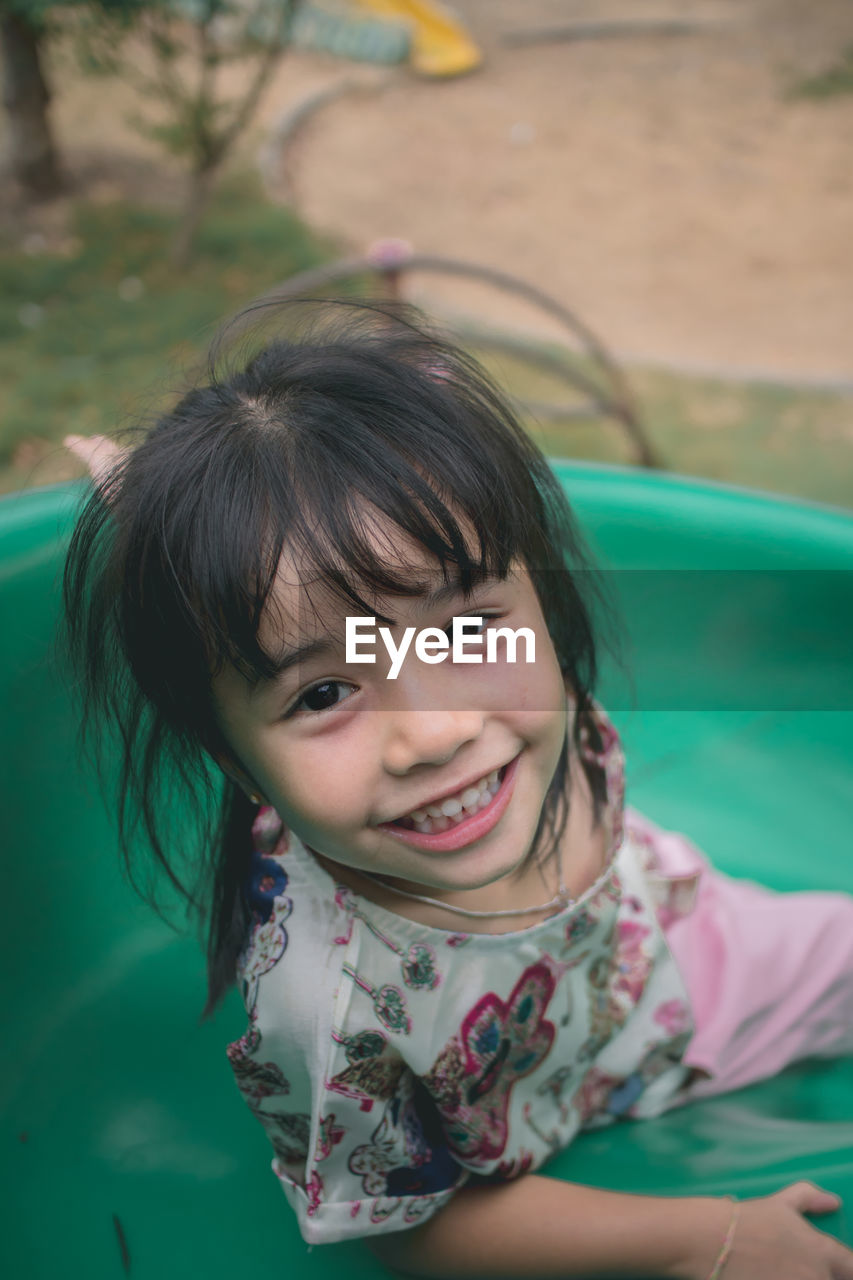 High angle portrait of cute smiling girl sliding in playground