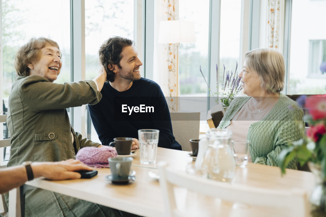 Smiling man sitting amidst senior women at dining table in retirement home