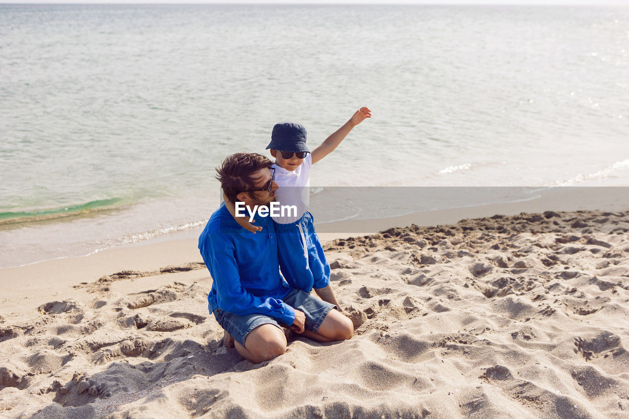 Dad and son in sunglasses play on the beach in summer in blue clothes while on vacation