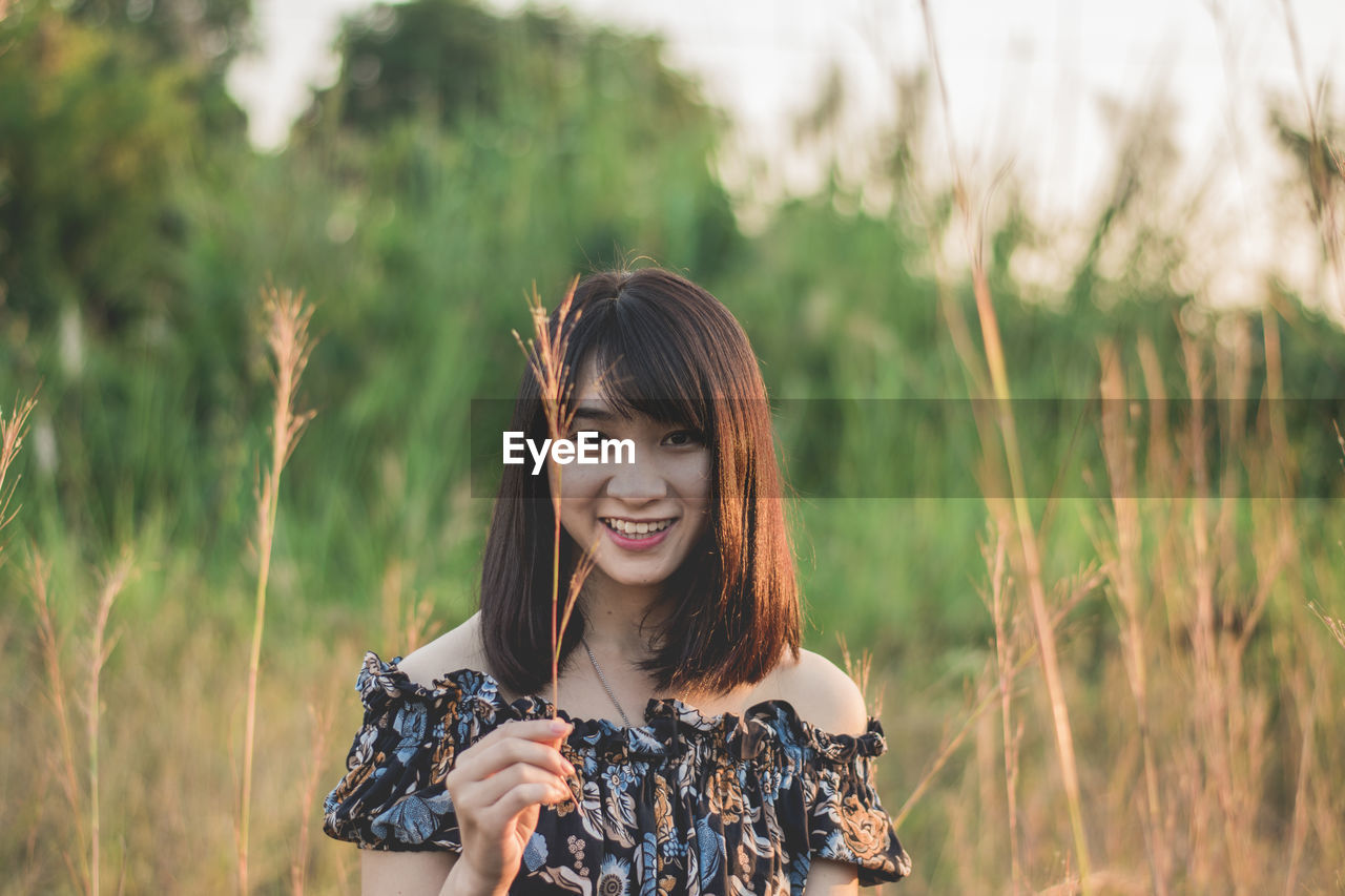 Portrait of young woman holding grass while standing on field