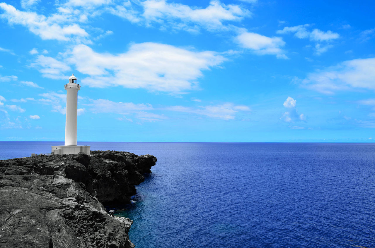 Lighthouse by sea against blue sky