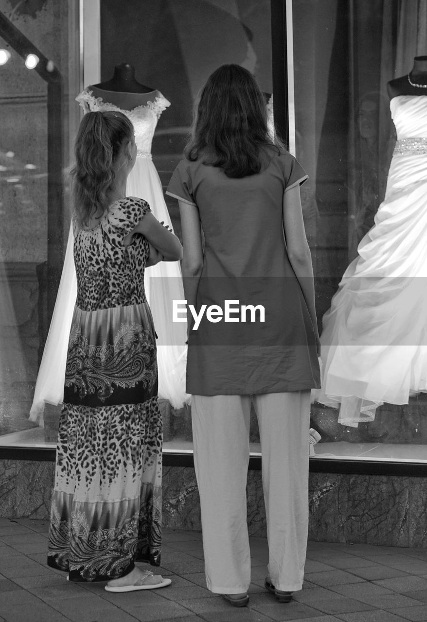 Rear view of friends standing in front of dress displayed in store