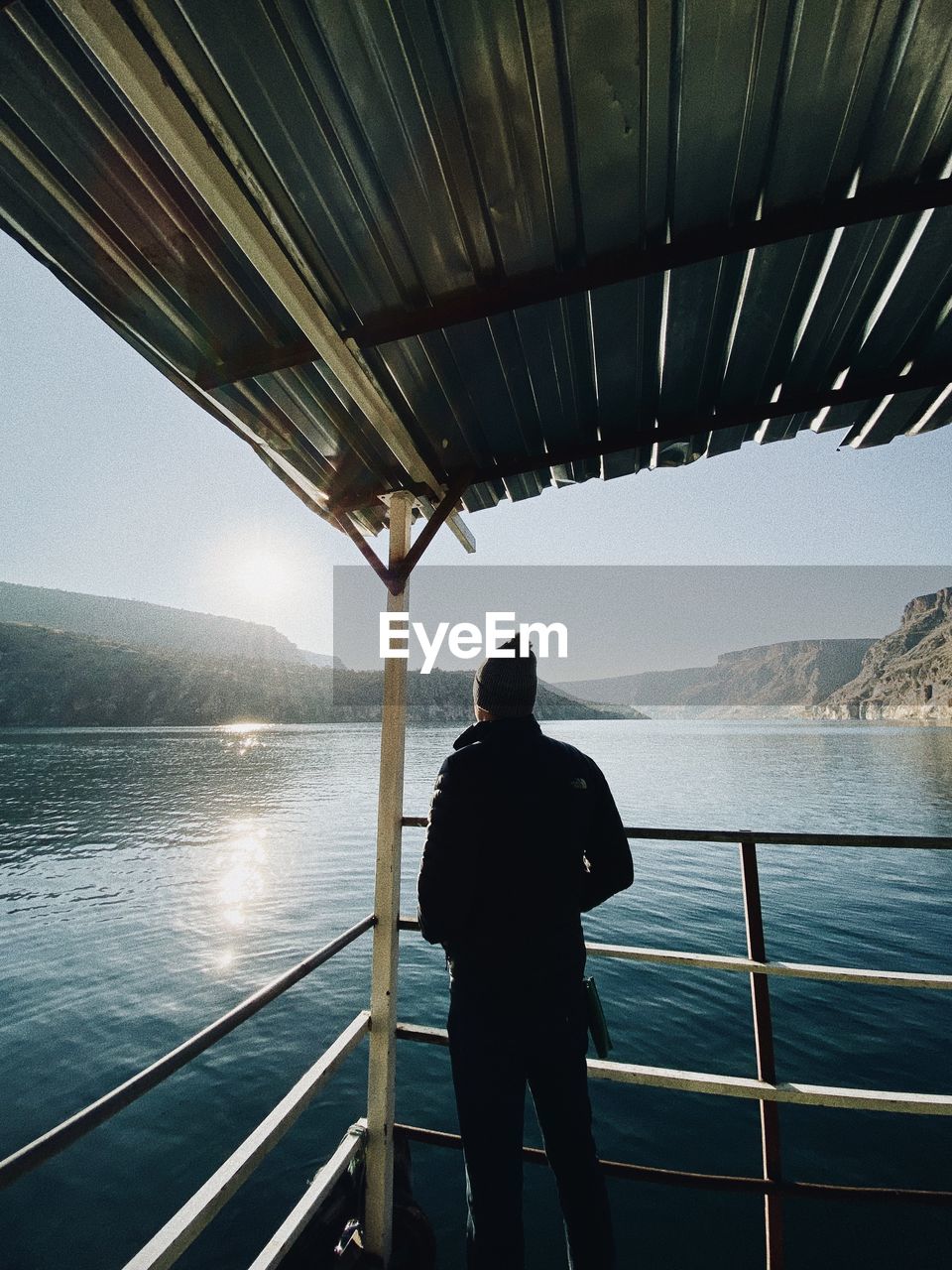 rear view of man standing by railing against sea