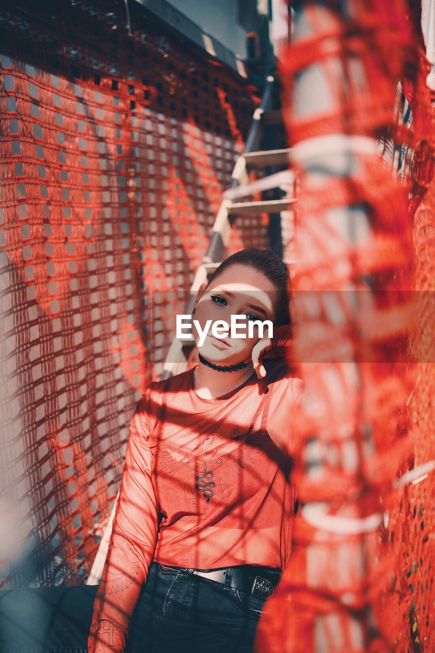 Portrait of young woman sitting on ladder amidst red net