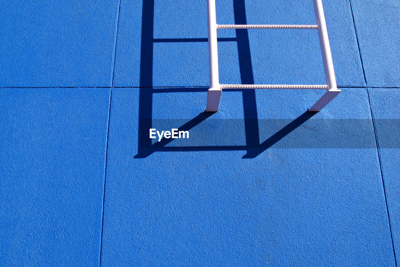 Low angle view of white ladder on blue wall during sunny day