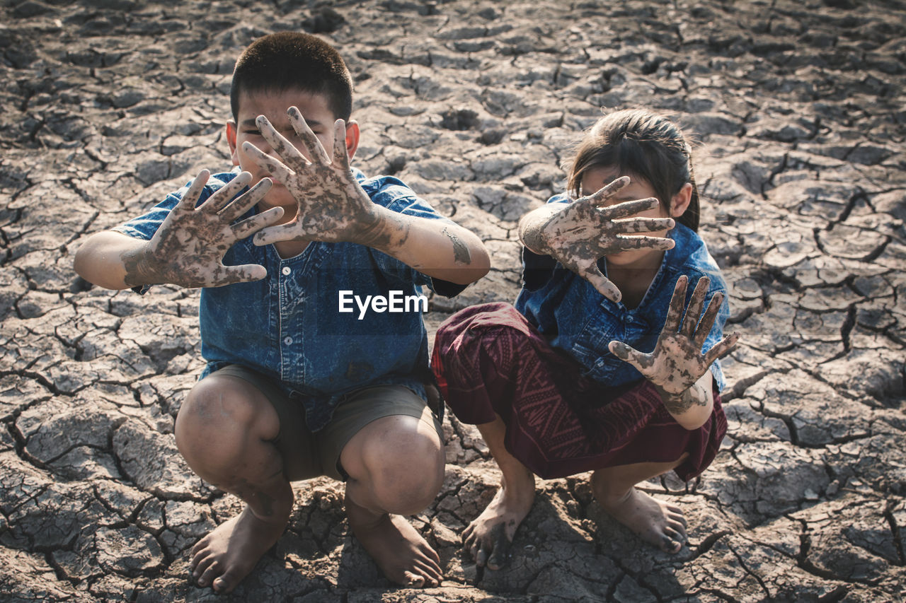 Siblings with messy hands gesturing while crouching on ground