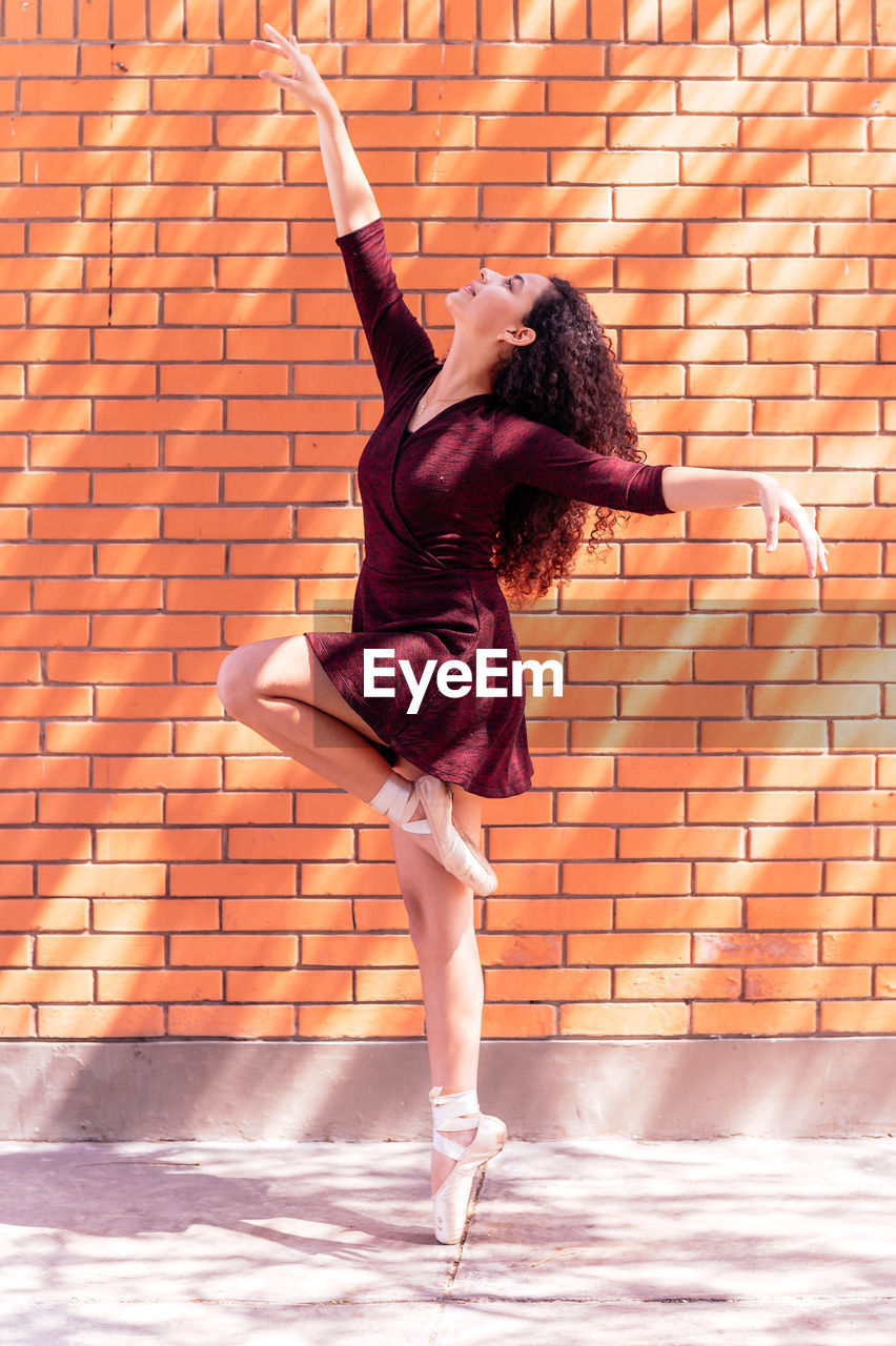 full length of young woman standing against brick wall