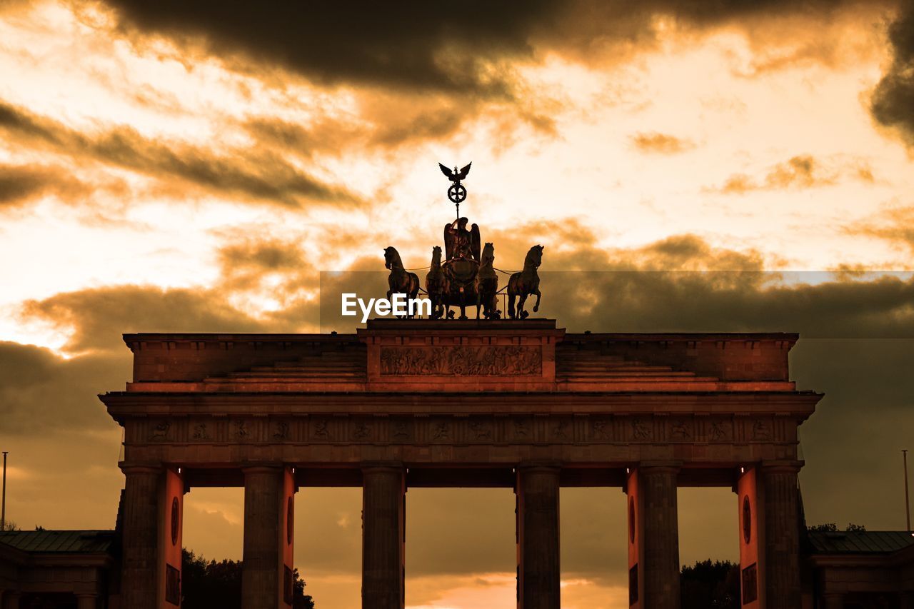 Low angle view of triumphal arch against cloudy sky