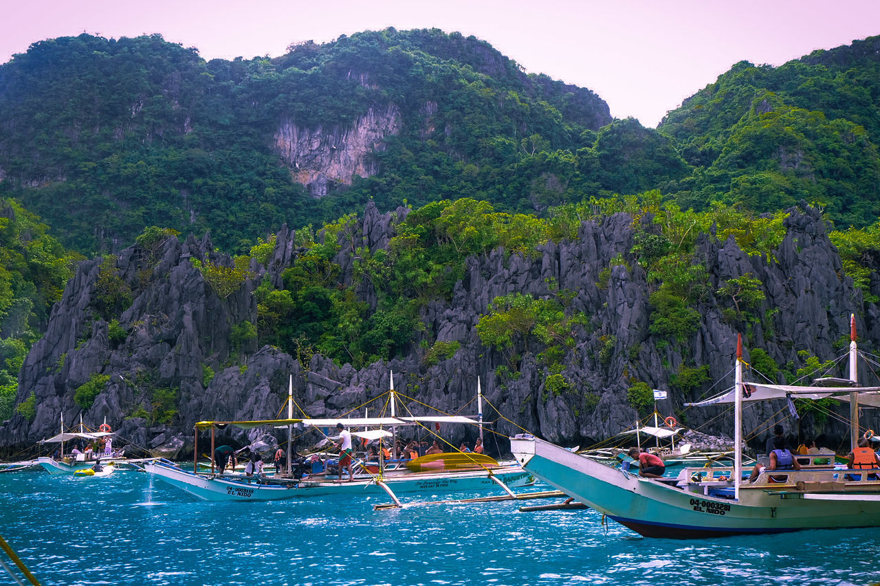 BOATS MOORED ON SEA AGAINST MOUNTAINS