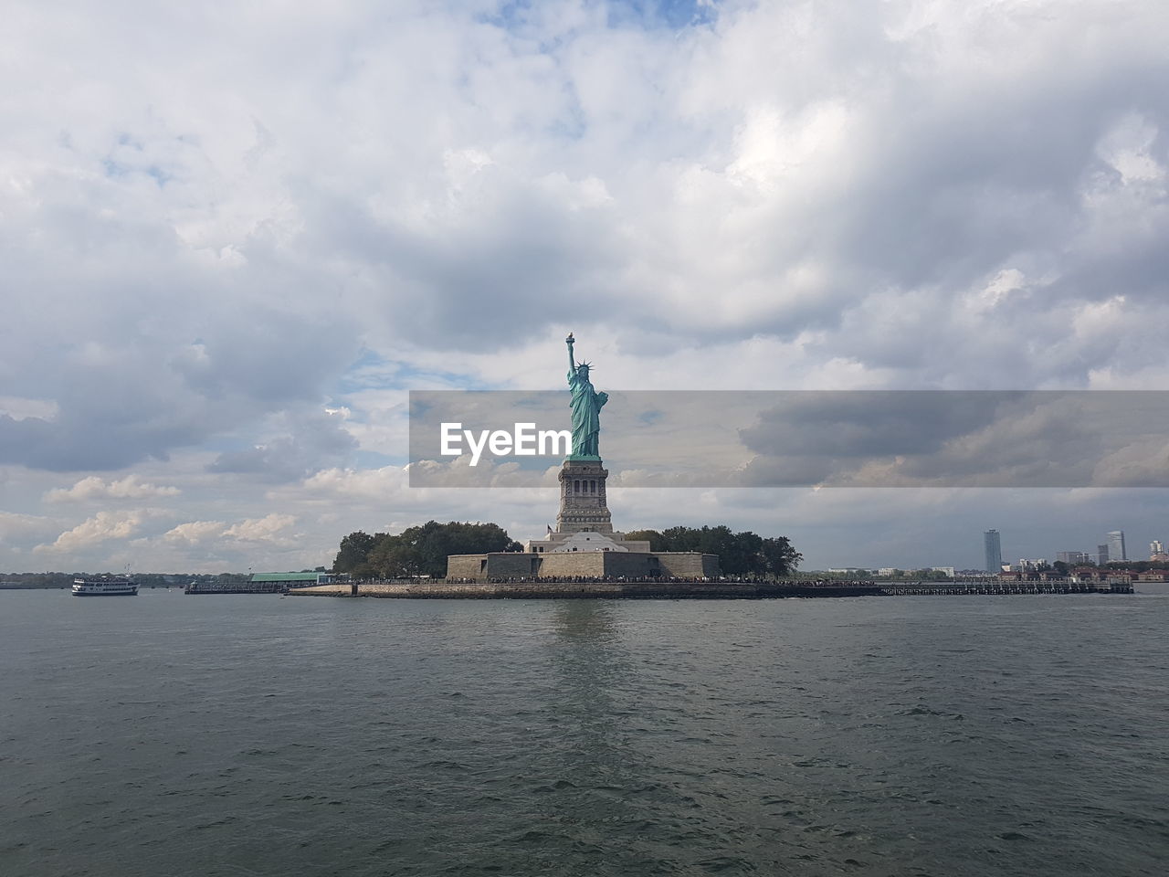 Statue of liberty by sea against cloudy sky