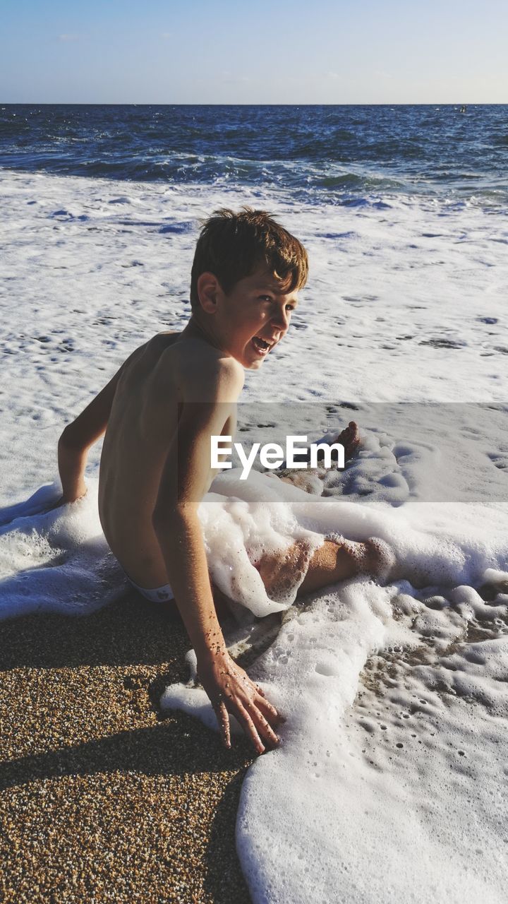 Shirtless boy sitting at beach